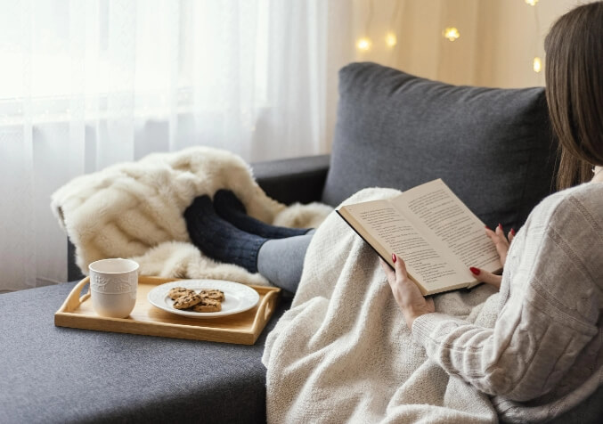 Woman Keeping Warm with blankets while Reading in Sofa