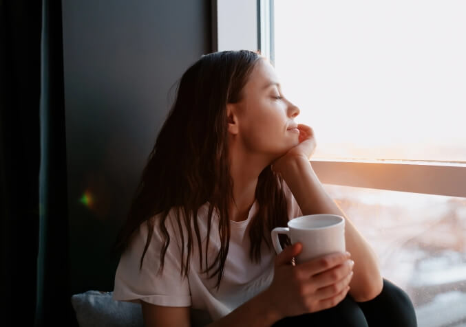 Woman Staring outside the window While Enjoying a Cup of Tea