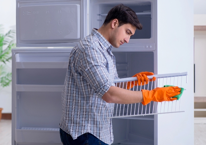 Man with Gloved hand while cleaning a rack from an empty fridge in the kitchen