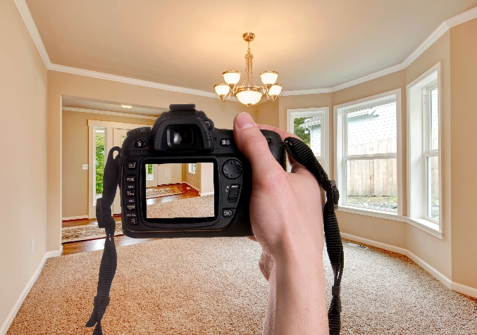 Hand holding a camera to take a photo of a carpeted section of the house