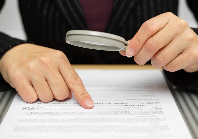 Two hands inspecting a document with magnifying glass