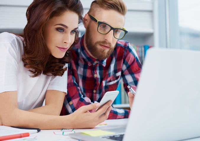 Couple looks at laptop while woman holds phone